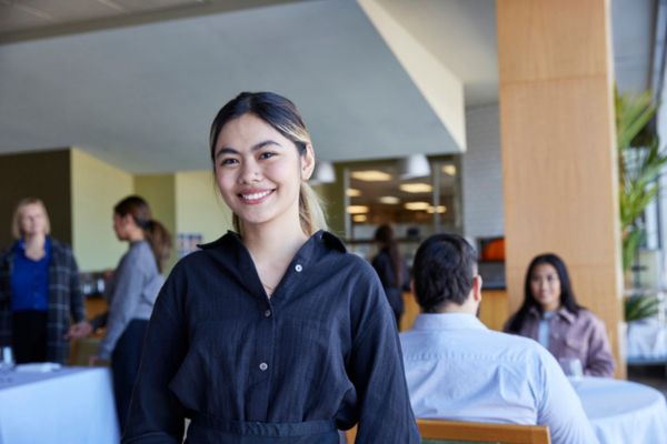Hospitality student standing in a restaurant setting and smiling